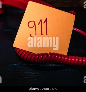 Writing 911 on memo post reminder.  sticky paper surrounded by wire of landline phone. Stock Photo