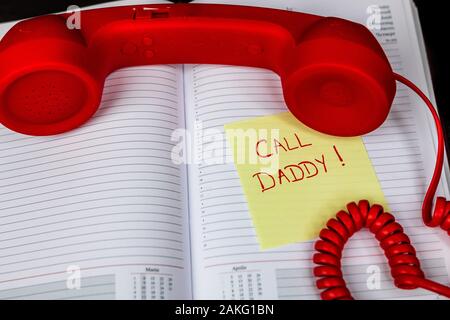 Writing Call daddy on memo post reminder.  sticky paper with text call daddy and landline phone. Stock Photo