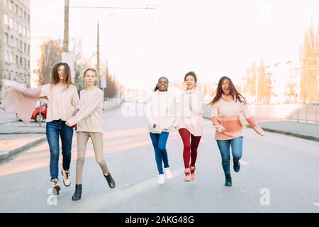 Multiracial group of friends from five young women runs and has a fun on city street. The concept of friendship and unity between different human race Stock Photo