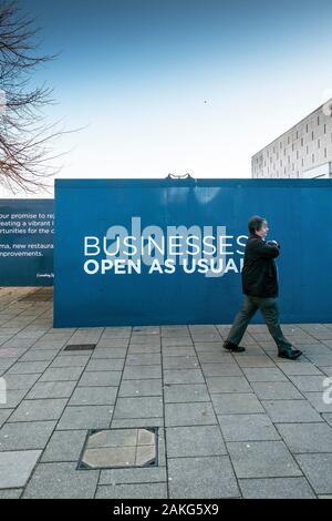 A pedestrian walking past hoardings around a demolition site in Basildon Town centre in Essex. Stock Photo