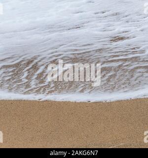 The foam of a small wave left behind on a beach as the wave recedes. Stock Photo