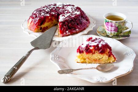 Cranberry tart, pie, cake piece, powdered sugar, white ceramic plate, tea spoon, cup of tea. Close up on white wooden table backgound view. Selective Stock Photo