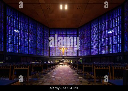 Symmetrical view of the interior of Kaiser Wilhelm Memorial church, with blue and purple glass blocks and a golden crucifix at the end of the aisle Stock Photo