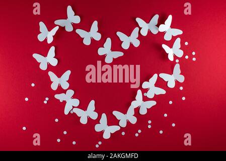 White butterflies of paper in shape of heart on red background for happy san valentine day. Stock Photo