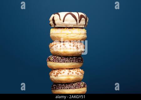 Stack of assorted delicious colorful donuts near dark blue background, sugar concept Stock Photo