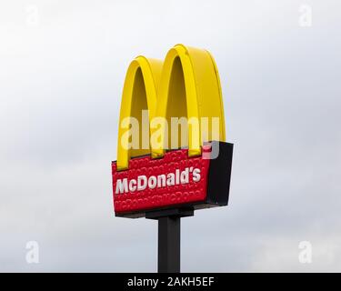 Junction One Retail Park, Rugby, Warwickshire, UK: McDonalds restaurant sign on a black pole against a light grey sky. Stock Photo