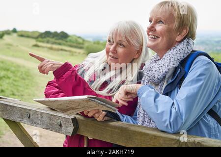 Two Senior Women Friends On Walking Holiday Resting On Gate With Map Stock Photo