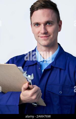 Studio Portrait Of Male Engineer With Clipboard And Spanner Against White Background Stock Photo
