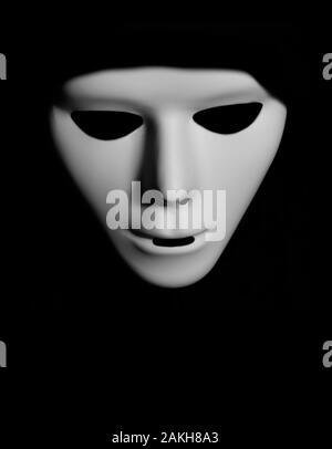 Scary white mask in the dark. Spooky guy in white masquerade. Black, invisible eyes. Black hood. Halloween style. Stock Photo