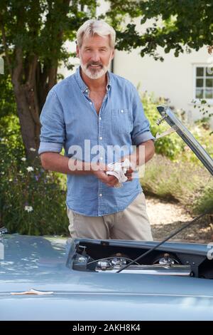 Portrait Of Mature Man Working On Engine Under Hood Of  Restored Classic Sports Car Outdoors Stock Photo