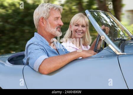 Mature Couple Enjoying Road Trip In Classic Open Top Sports Car Together Stock Photo