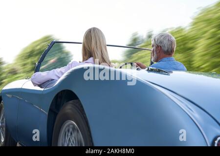 Rear View Of Mature Couple Enjoying Road Trip In Classic Open Top Sports Car Together Stock Photo