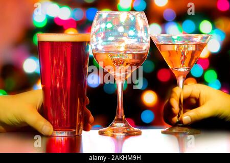 A close up of a couple of people's hand with a beer, wine and a martini and colourful lights on the background Stock Photo