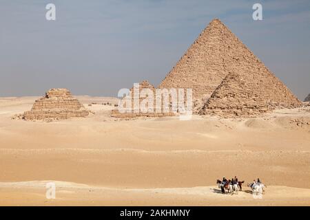 People ride horses through the desert sand on Giza Plateau near the Great Pyramids of Egypt Stock Photo