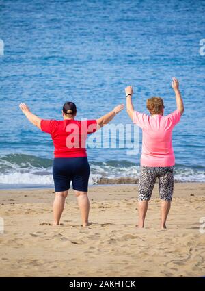 Rear view of elderly obese woman exercising on beach. Stock Photo