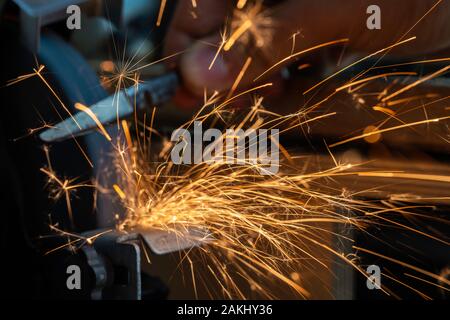 Sparks fly out of the grinder during use. A knife is sharpened on the grinder. Stock Photo