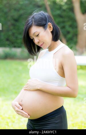 Beautiful pregnant of portrait asian young woman relax in the park, girl with belly standing on grass and yoga exercise for wellness, copy space. Stock Photo