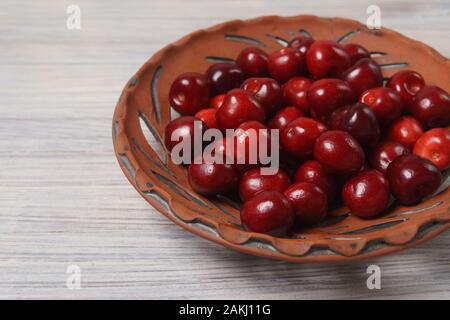Red sweet cherries in a clay dish on a white wooden table Stock Photo