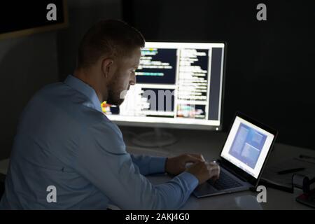 Programmer Working Late At Night On Multiple Computer Screens Stock Photo