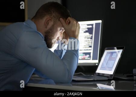 Worried Programmer Working Late At Night On Multiple Computer Screens Stock Photo