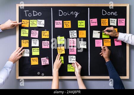 Group Of People Writing On Sticky Notes Attached To Blackboard In Office Stock Photo