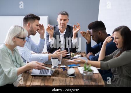 Businessman Meditating While His Colleagues Having Conversation In Office Stock Photo