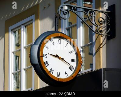 exterior wall detail with large suspended wall clock. steel bracket. white dial face & roman numeral numbers. clock style depicting modern wrist watch Stock Photo