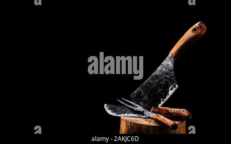 Rustic butcher meat knife, cleaver and fork on black background Stock Photo