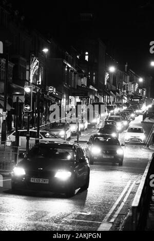 Cars Travelling Down a Hill in a Town Centre with Bright Headlights, Harrogate, North Yorkshire, England, UK. Stock Photo