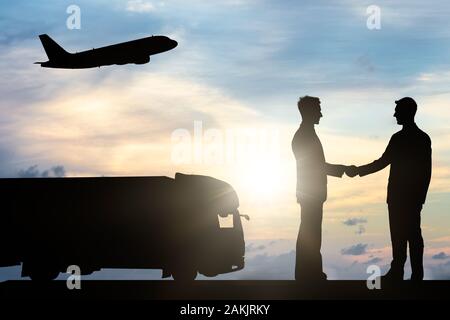 Silhouette Of Two Businessmen Shaking Hands Near Commercial Truck And Aero Plane During Sunset Stock Photo