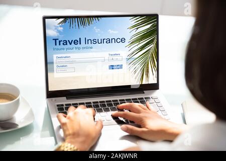 Person Using Laptop Over Office Desk Working On Travel Insurance Application For Trip Stock Photo