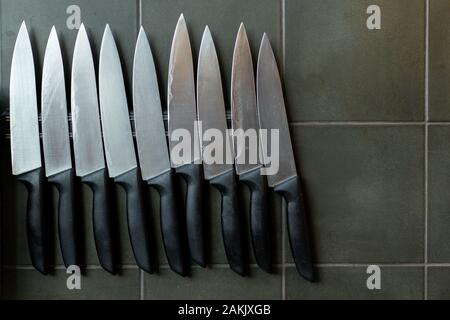 Magnetic holder with set of knives on grey stone background Professional kitchen metal knives are hanging on a magnetic holder on the wall with dark g Stock Photo