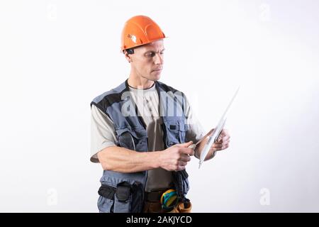 The builder is cleaning a spatula. In work clothes and hard hat. On a light gray background. Stock Photo