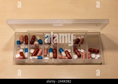 Plastic pill box containing pharmaceutical drugs in form of tablets, pills and capsules on a birch table Stock Photo