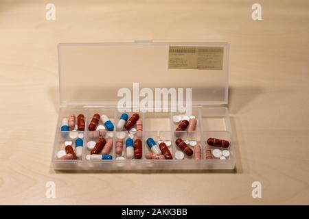 Plastic pill organizer with pills, tablets and capsules on a birch table Stock Photo