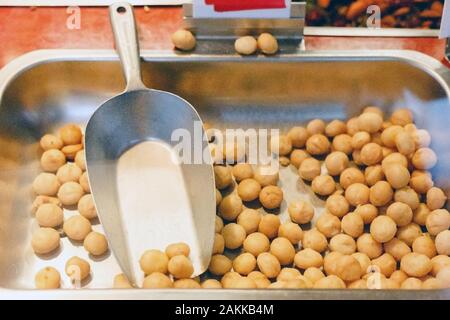 Fresh raw organic macadamia nuts for sale at farmers market in store showcase with a scoop at farmers market. Vegan food, healthy nutrition, keto food Stock Photo