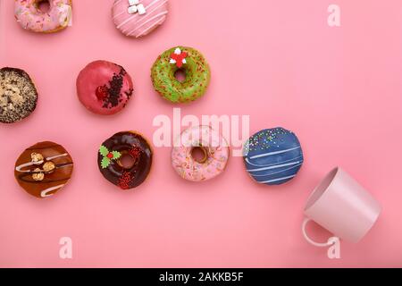 Colorful Donuts with icing and coffe cups on pastel rose background. Sweet donuts. Flat lay Stock Photo