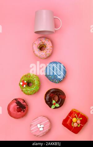 Colorful Donuts with icing and coffe cups on pastel rose background. Sweet donuts. Flat lay Stock Photo