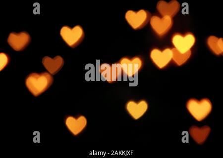 Black background with bright warm heart shaped bokeh lights. Holiday, Valentines Day background. Ideal to layer with any design. Horizontal Stock Photo