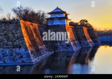 ANcient samurai shogun castle in Osaka surrounded by moat with water and powerful stone walls facing rising sun with watch tower. Stock Photo