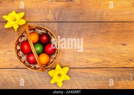Seven colourful Easter eggs in pastel colours in the basket and two yellow daffodils on vintage reclaimed oak background, top view Stock Photo