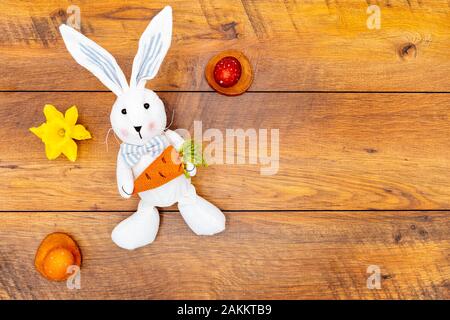 Colourful wax painted Easter eggs in pastel colours on wooden pads, daffodil and Easter bunny with carrot on vintage reclaimed oak background top vie Stock Photo