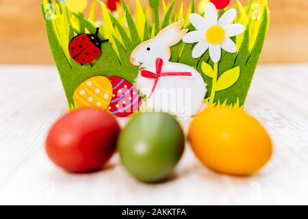Closeup of three blurred colourful Easter eggs in front of decorative felt basket on white painted vintage reclaimed oak background, front view Stock Photo