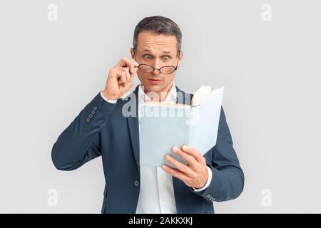 Freestyle. Mature businessman in eyeglasses standing isolated on white looking at book page surprised Stock Photo