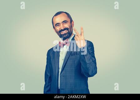 Smiling, bearded businessman showing number two, peace, victory sign with fingers hand gesture. Companion, couple, pair. Confident standing man with d Stock Photo