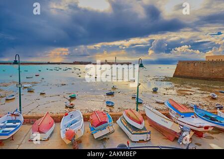 Sunset vs storm clouds, colored landscape of boats on the shore of atlantic ocean in Cadiz Stock Photo