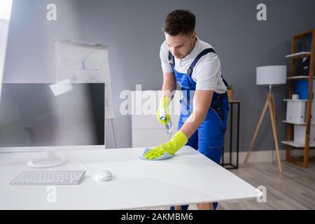 Portrait Of Happy Young Maid Cleaning Glass Table In Office Stock Photo