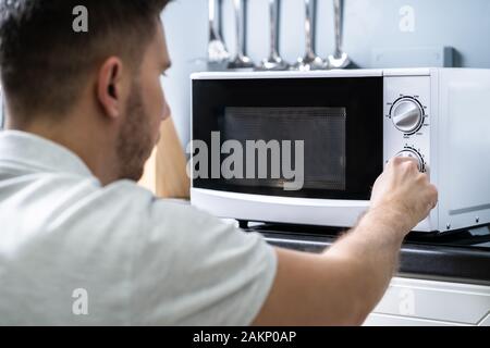 Young Man Preparing Food In Microwave Oven On Kitchen Counter Stock Photo