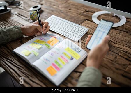 Close-up Of Businessman Writing Schedule In Calendar Diary On Desk Stock Photo