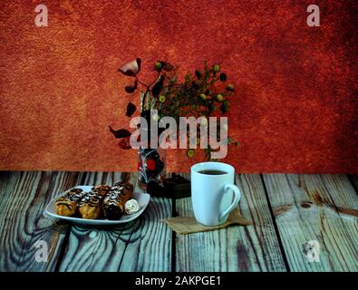 Warm autumn still life, a mug of hot tea, a plate with eclairs and a vase with a herbarium. Close-up. Stock Photo